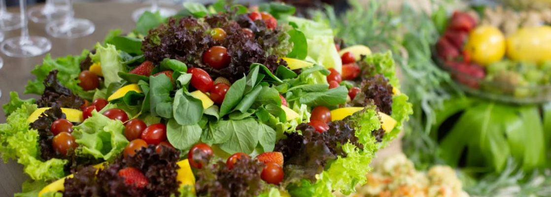 Colorful mixed salad with leafy greens, cherry tomatoes, and mango slices on a buffet table.