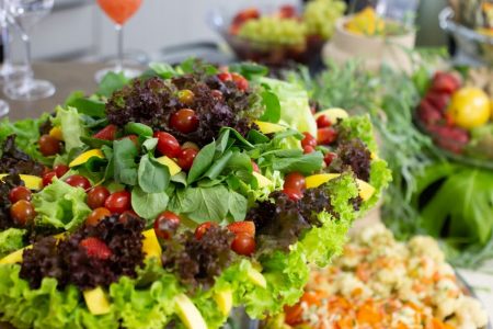 Colorful mixed salad with leafy greens, cherry tomatoes, and mango slices on a buffet table.