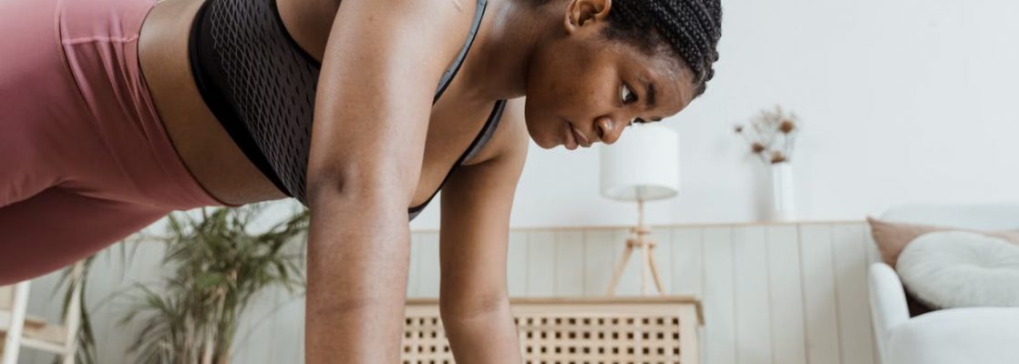 Woman with braided hair doing push-ups indoors, focusing on fitness and strength.